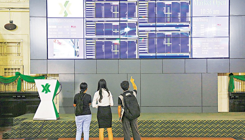 A file photo shows people monitoring stock prices and the index displayed on a large video screen at the Yangon Stock Exchange in Yangon on March 20, 2020. Global stock markets rose on Monday, boosted by hopes of a US stimulus package that helped to offset American-China tensions ahead of key trade talks this week.— AFP photo