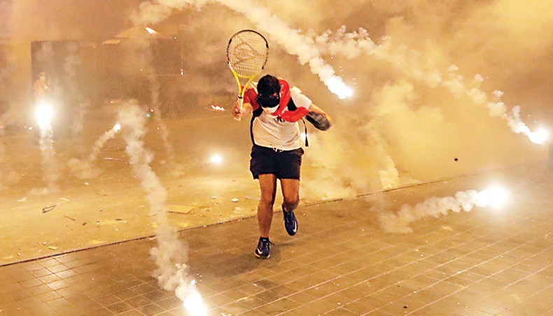 A Lebanese protester, enraged by a deadly explosion blamed on government negligence, runs from tear gas canisters fired by security forces amid clashes for the second evening near an access street to the parliament in central Beirut on Sunday. — AFP photo