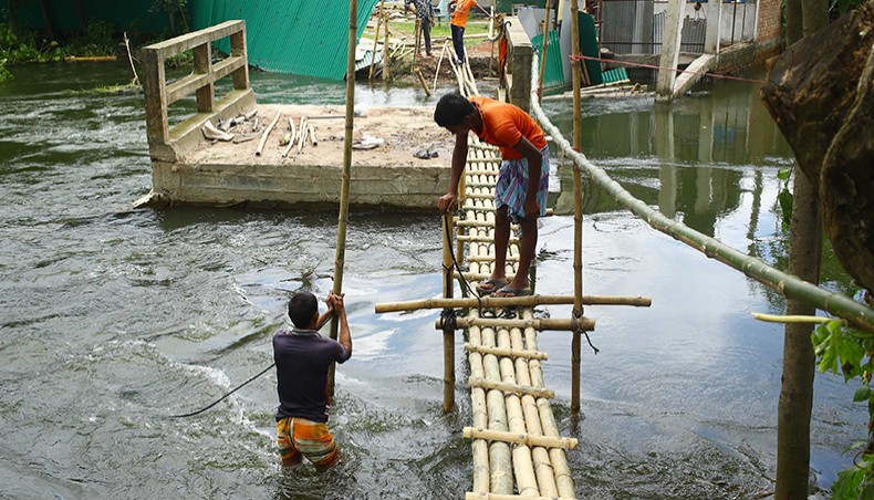 Local people on Wednesday set up a makeshift bamboo bridge linking a culvert to an approach road, part of which got washed away by floodwater at Mograkanda in Savar near the capital city. — Sourav Lasker