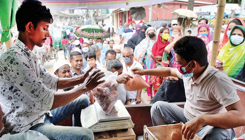 A salesperson weighs onions and another salesperson hands over red lentil to a customer standing in queue at a Trading Corporation of Bangladesh-run open market sales point at Shantinagar in the capital on Sunday. — New Age photo