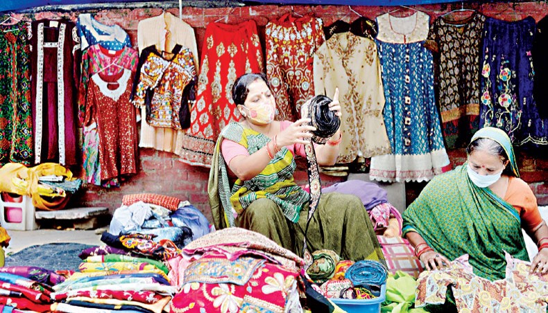 Women vendors, wearing face masks as a preventive measure against the COVID-19 coronavirus, adjust garments at their roadside shop in New Delhi on September 26. — Agence France-Presse/Sajjad Hussain