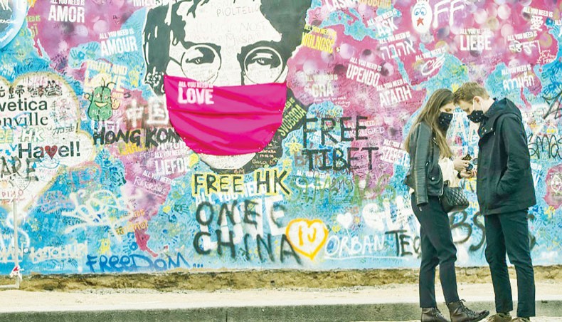 In this file photo taken on April 6, 2020 a couple stand in front of the ‘Lennon Wall’ with a face mask attached to the image of John Lennon in Prague.— AFP photo