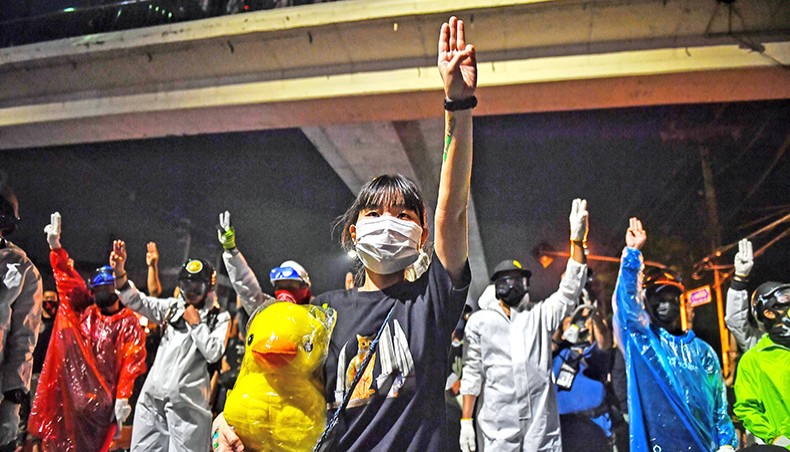 Pro-democracy protesters, including one carrying a stuffed toy duck, give the three-finger salute during an anti-government rally outside the 11th Infantry Regiment in Bangkok on Sunday. — AFP photo
