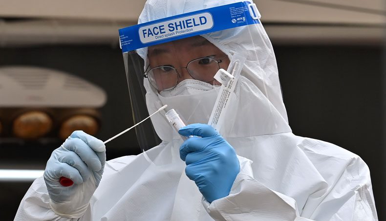 A medical staff member wearing protective gear takes a swab from a visitor to test for COVID-19 at a temporary testing station outside the City Hall in Seoul on December 28, 2020. — AFP photo