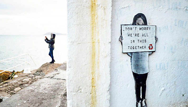 A woman takes a picture of the sea next to a shelter with an artwork that says ‘Don’t worry, we’re all in this together’ near Dublin, Ireland, on January 5, 2021. — PA Images/NurPhoto/Artur Widak