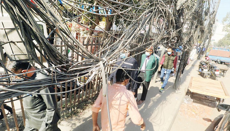 Overhead TV and internet cables loosely hang over a footpath hampering pedestrian movement at Gulshan in Dhaka on Friday. — New Age photo