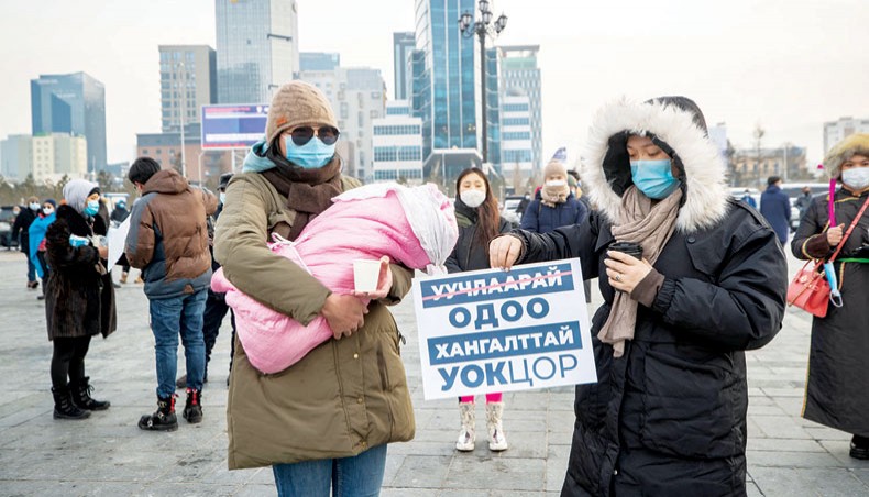 A protester carrying a 2-month-old baby while another holds a sign urging officials of the national emergency commission to resign, during a rally at Sukhbaatar square in Ulaanbaatar, the capital of Mongolia on Thursday. — AFP photo