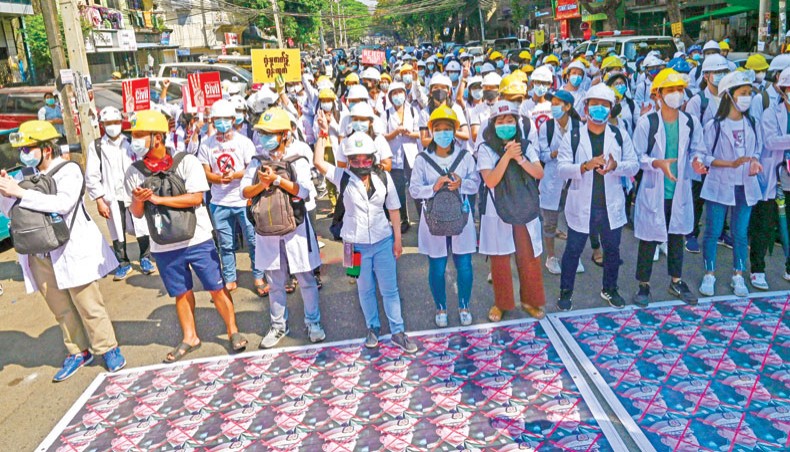 Medical personnel and students stand before the portraits of Myanmar armed forces chief Senior General Min Aung Hlaing placed on a street during a demonstration against the military coup in Yangon on Friday. — AFP photo