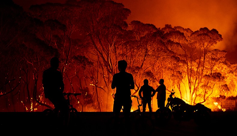Residents look on as wildfires burn through bush on January 4, 2020 in Lake Tabourie, Australia. — Common Dreams/Getty Images/Brett Hemmings
