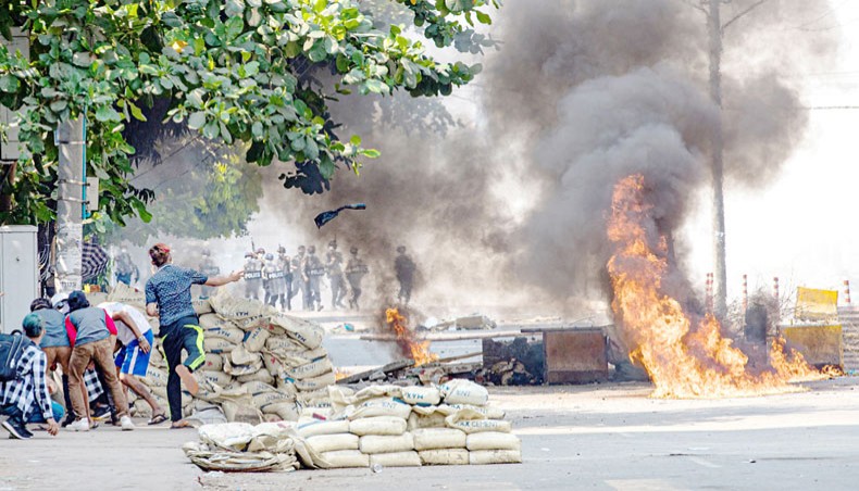 A protester, fifth from left, throws a projectile towards security forces as others shelter behind a barricade during a crackdown on protests against the military coup in Yangon on March 17. — Agence France-Presse/STR