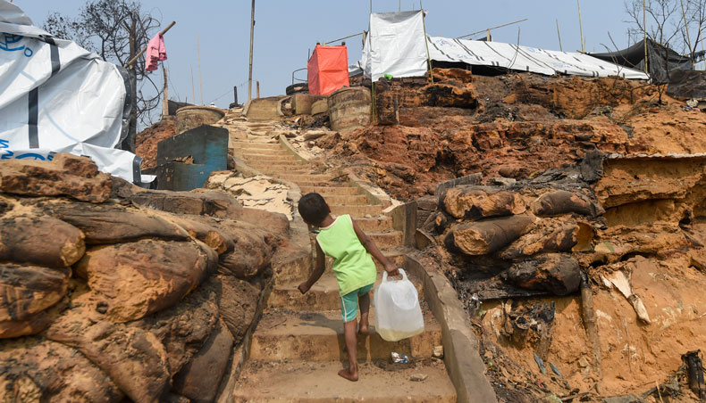 A Rohingya refugee child carries water to her temporary shelter days after a fire burnt their home at a refugee camp in Ukhia, in the south-eastern Cox’s Bazar district on March 25, 2021. — AFP photo