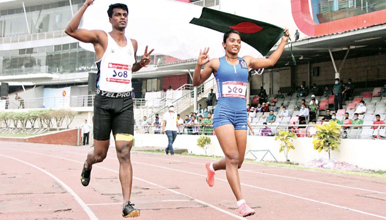 Bangladesh navy athletes Mohammad Ismail (L) and Shirin Akhter give lap of honour after emerging champions in the men’s and women’s 100metre sprint events of the Ninth Bangabandhu Bangladesh Games at the BNS on Saturday.— Courtesy photo