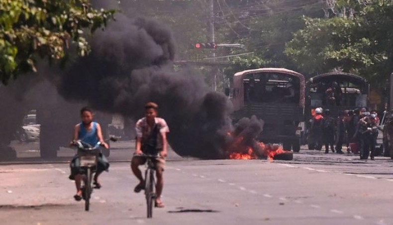 Cyclists pass police standing next to a burning makeshift tyre barricade, erected by protesters demonstrating against the military coup, in Yangon’s South Okkalapa township on April 1, 2021. — AFP photo