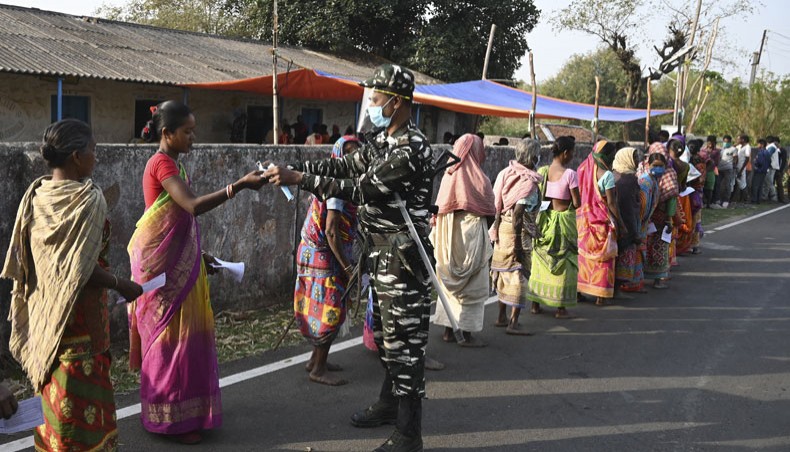 A paramilitary personnel distributes facemasks to voters standing in queue to cast their ballots outside a polling station during Phase 1 of West Bengal's legislative election in Purulia district on March 27, 2021. — AFP file photo