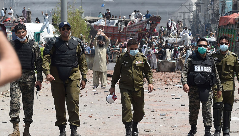 Security personnel walk back after having a talk with the supporters of Tehreek-e-Labbaik Pakistan party during a protest along a blocked street after their party’s leader was detained following his calls for the expulsion of the French ambassador, in Lahore on April 18, 2021. — AFP photo