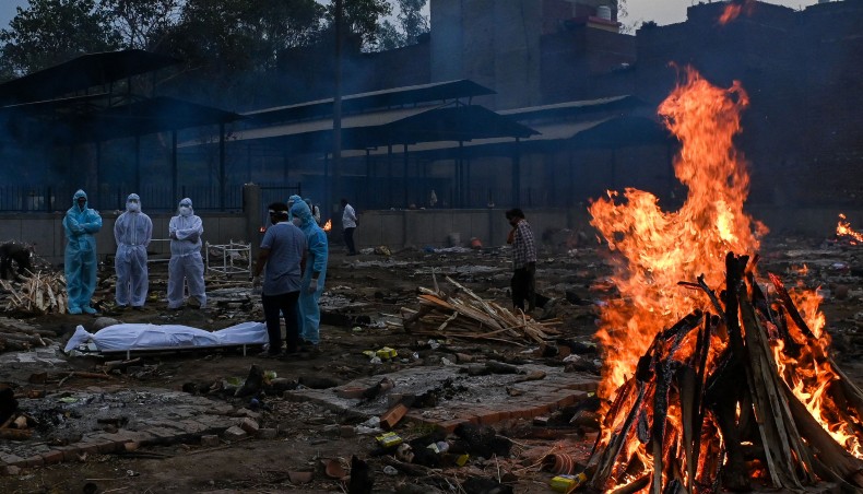 Relatives in personal protective equipment suits stand near the body of a person who died due to the Covid-19 coronavirus, at a cremation ground in New Delhi on May 6, 2021. — AFP photo
