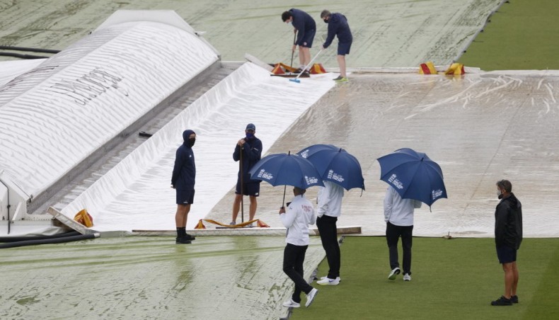 Umpires shelter under umbrellas to inspect the pitch as ground staff work after rain disrupted play on the third day of the first Test between England and New Zealand at Lord's on Friday. — AFP photo