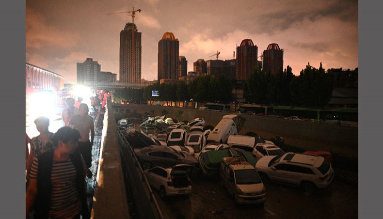 People look at cars stacked on each other at an entrance of a tunnel following a heavy rain in Zhengzhou in China's Henan province on July 21, 2021. — AFP